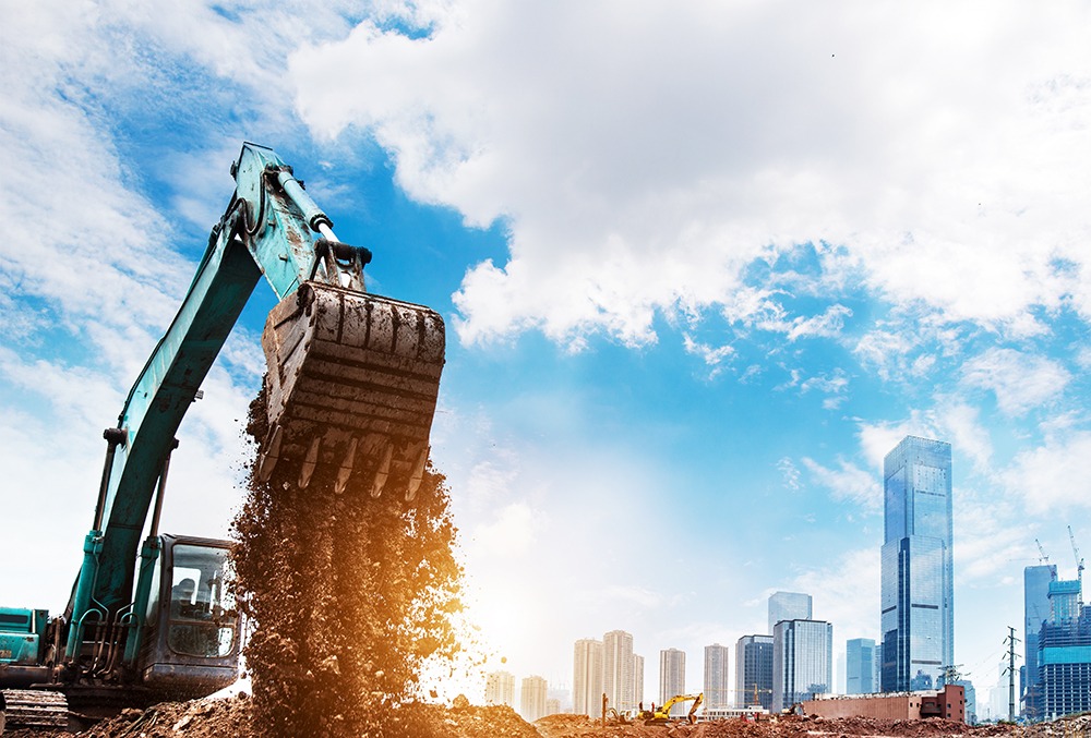 An excavator scooping up dirt at a construction site in front of a modern city skyline.