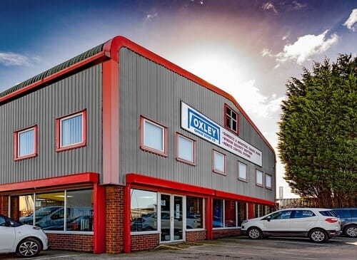 Exterior of Oxley Garage Doors Ltd. building with grey facade, red trim, and cars parked outside.