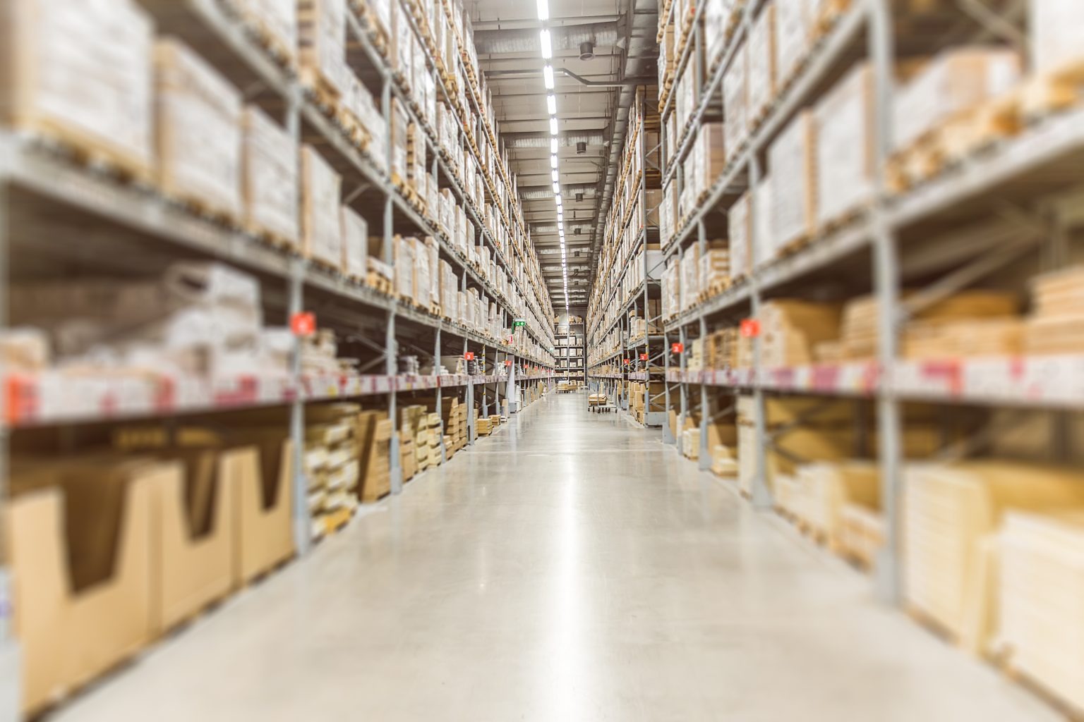 A view looking down a narrow, empty aisle in a modern warehouse, with packed metal shelving on both sides.