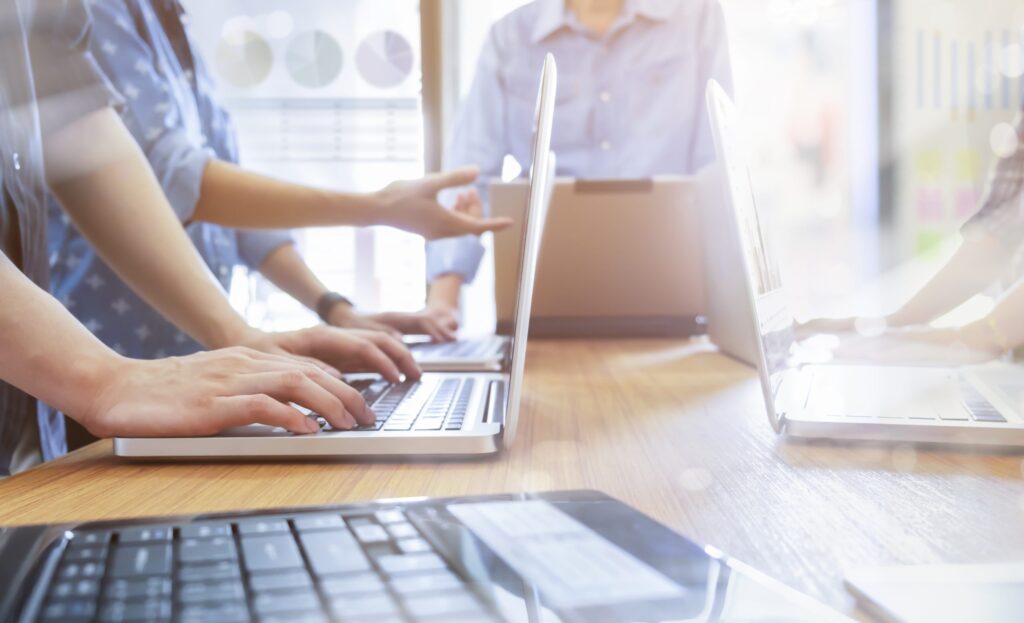 A team of people working on laptops during a meeting, with hands visible typing on the keyboards.