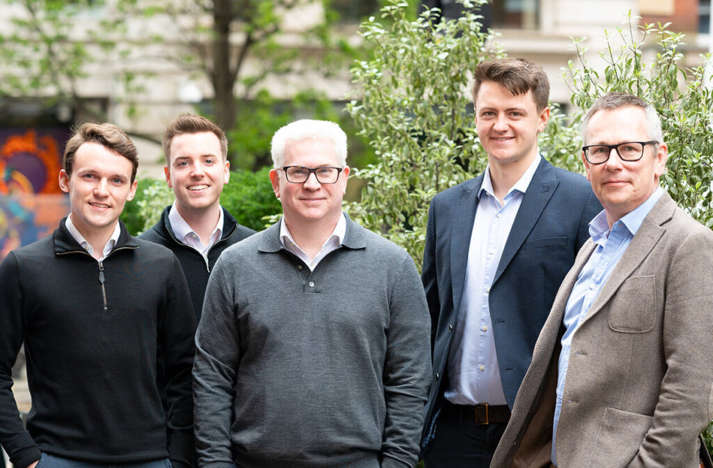 A group of smartly dressed men smiling at the camera in front of an office garden backdrop