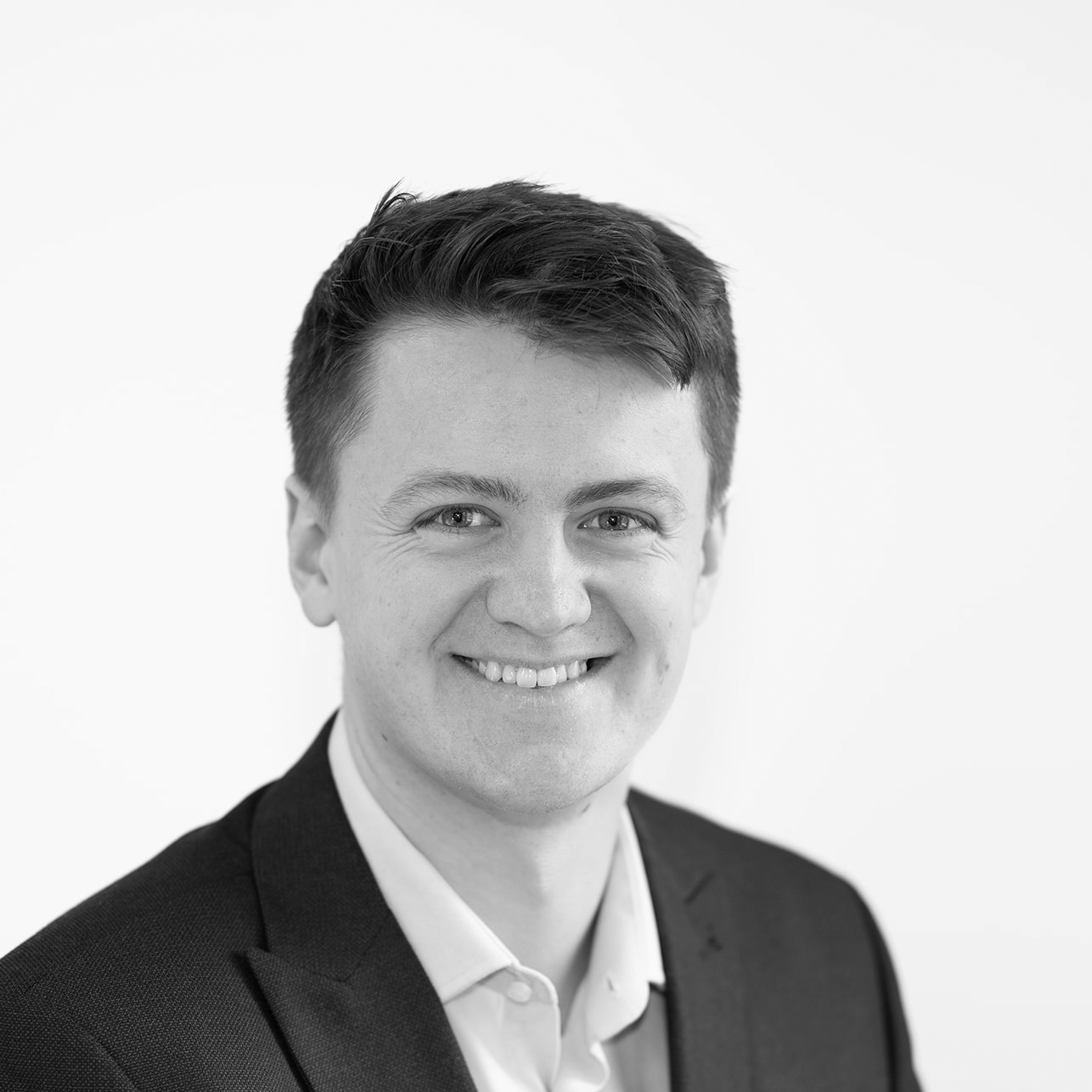 A black and white headshot image of a smiling man against a white backdrop