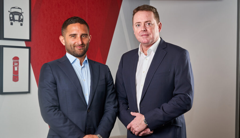 Two men wearing suits smiling at the camera in front of an office backdrop.