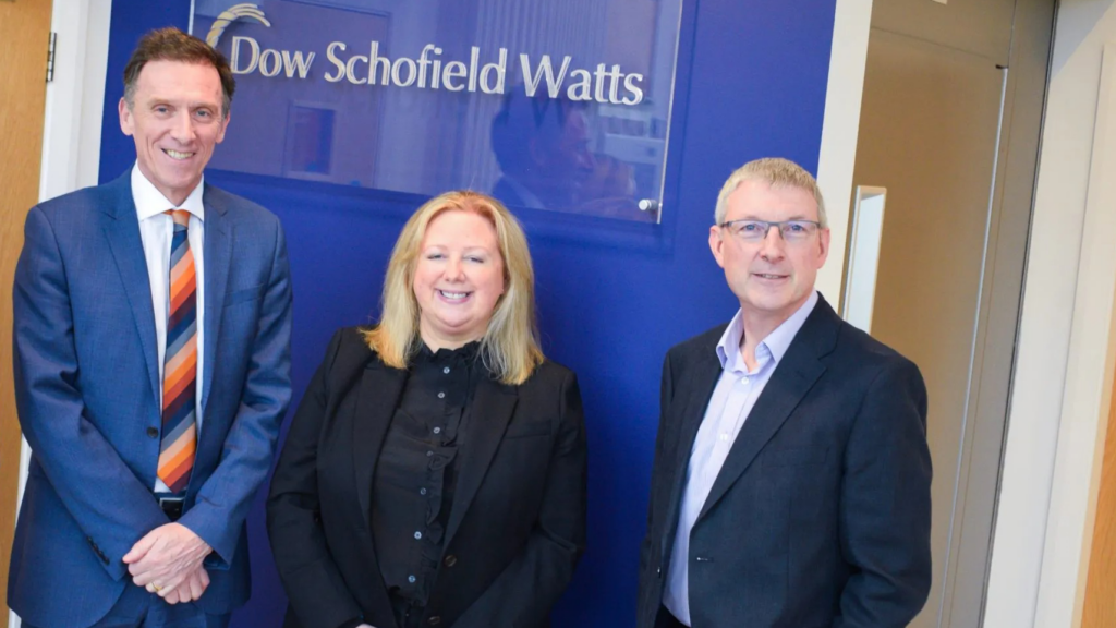An image of two smiling men and a woman in formalwear in front of the Dow Schofield Watts sign