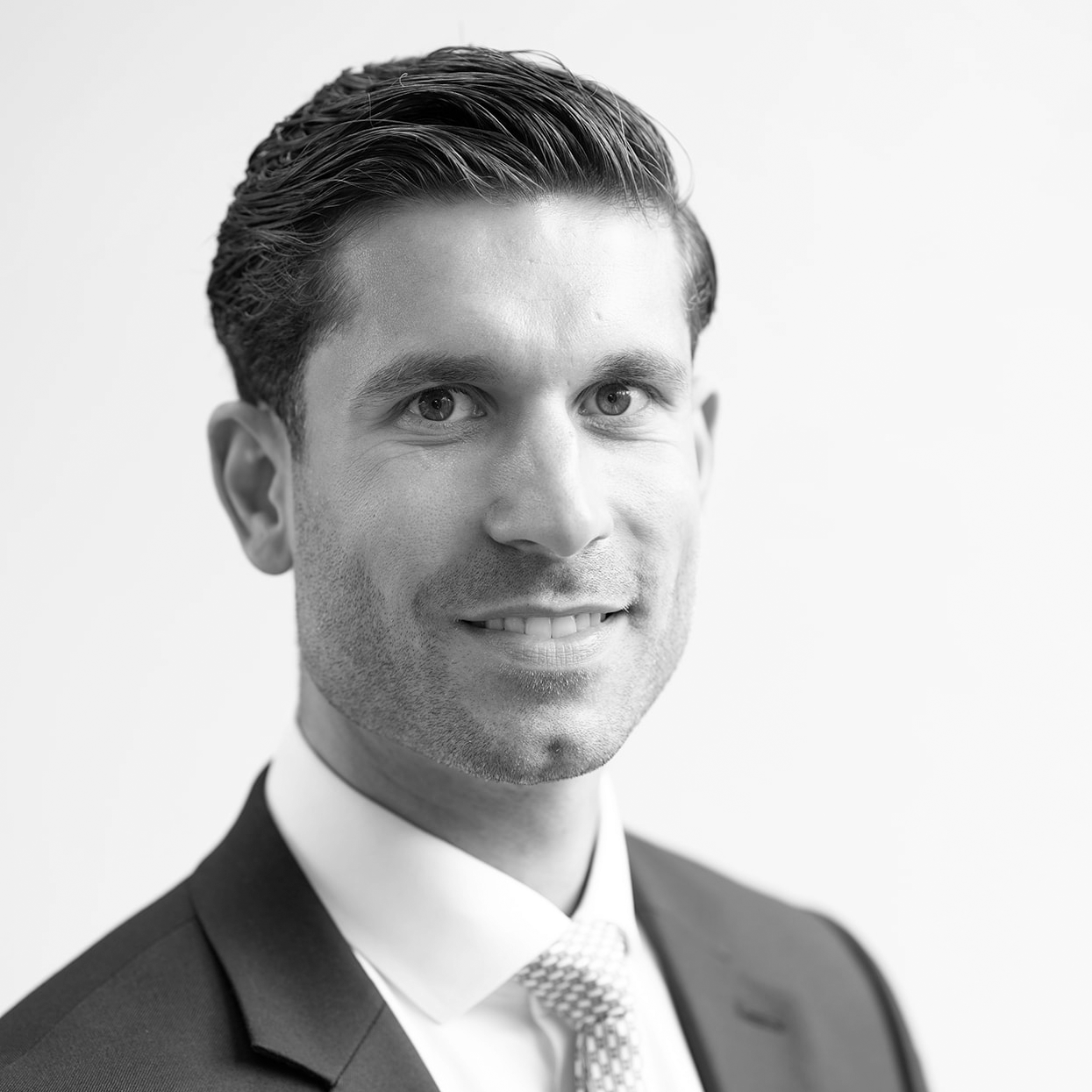 A black and white headshot image of a smiling man against a white backdrop