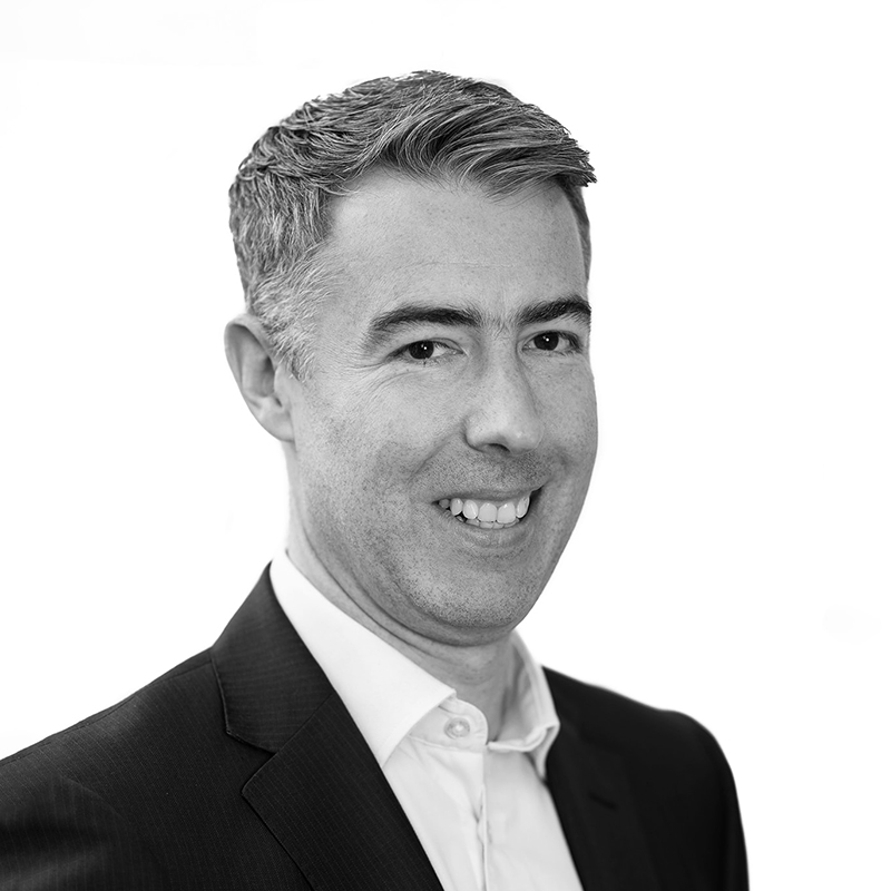 A black and white headshot image of a smiling man against a white backdrop