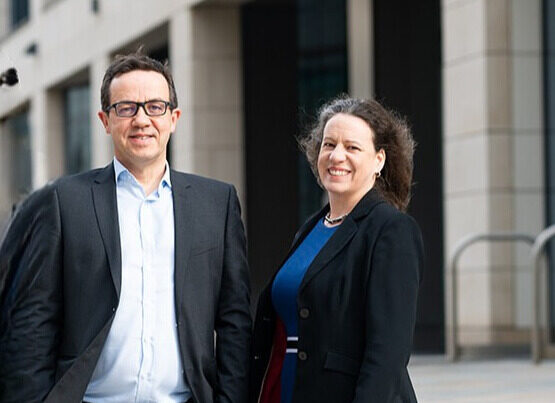 An image of a man and a woman in formalwear smiling at the camera in front of an office building