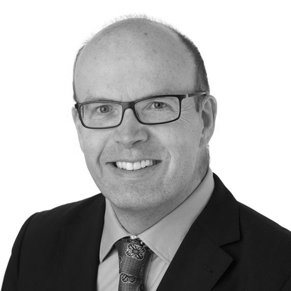 A black and white headshot image of a smiling man against a white backdrop