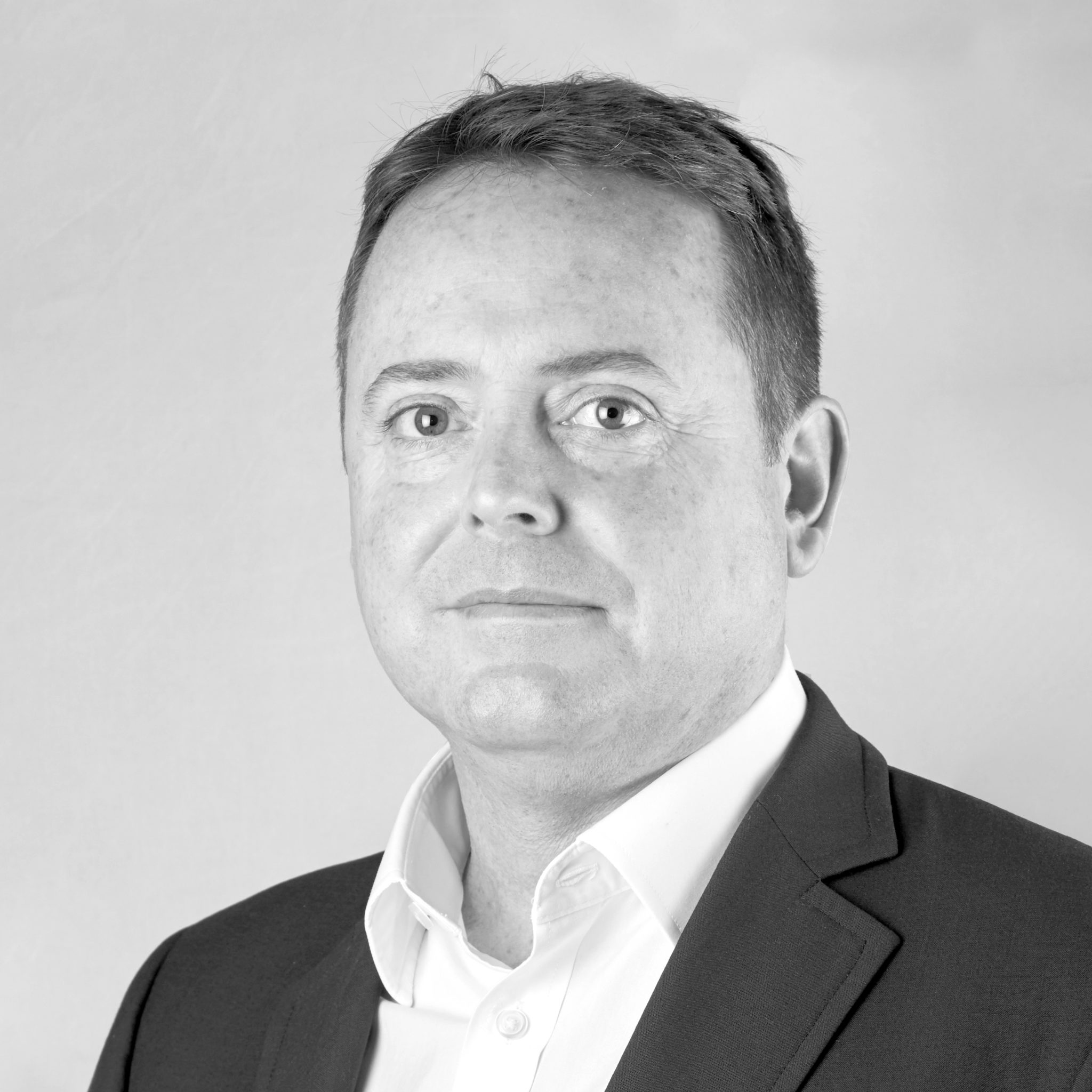A black and white headshot image of a smiling man against a white backdrop
