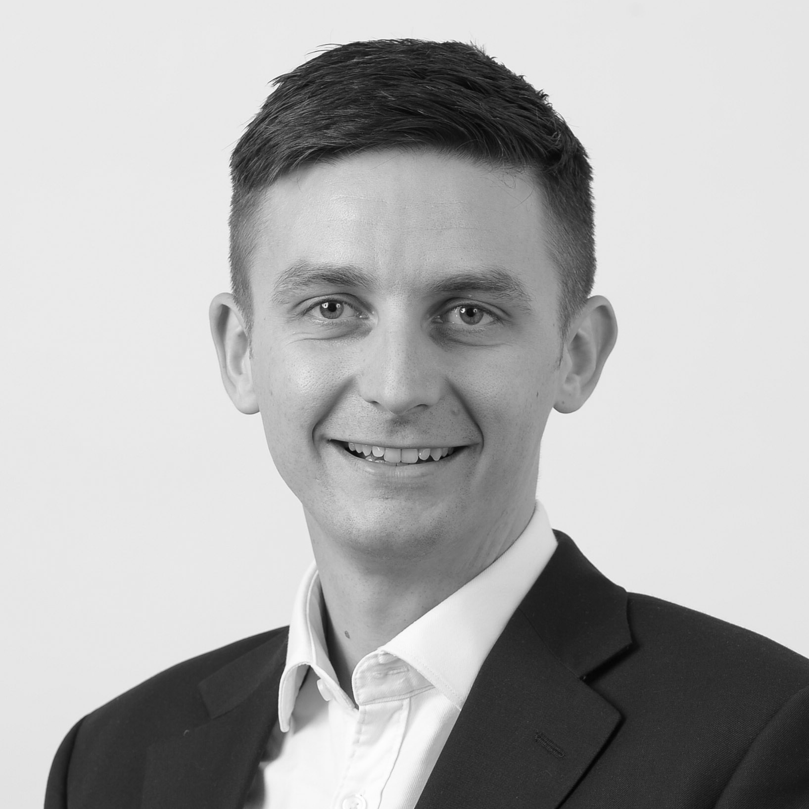 A black and white headshot image of a smiling man against a white backdrop