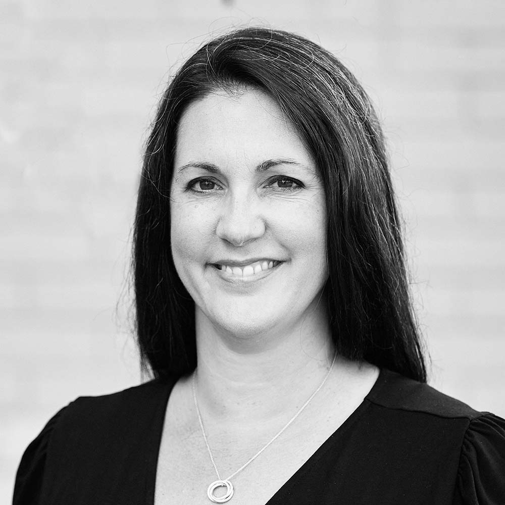A black and white headshot image of a smiling woman against a white backdrop