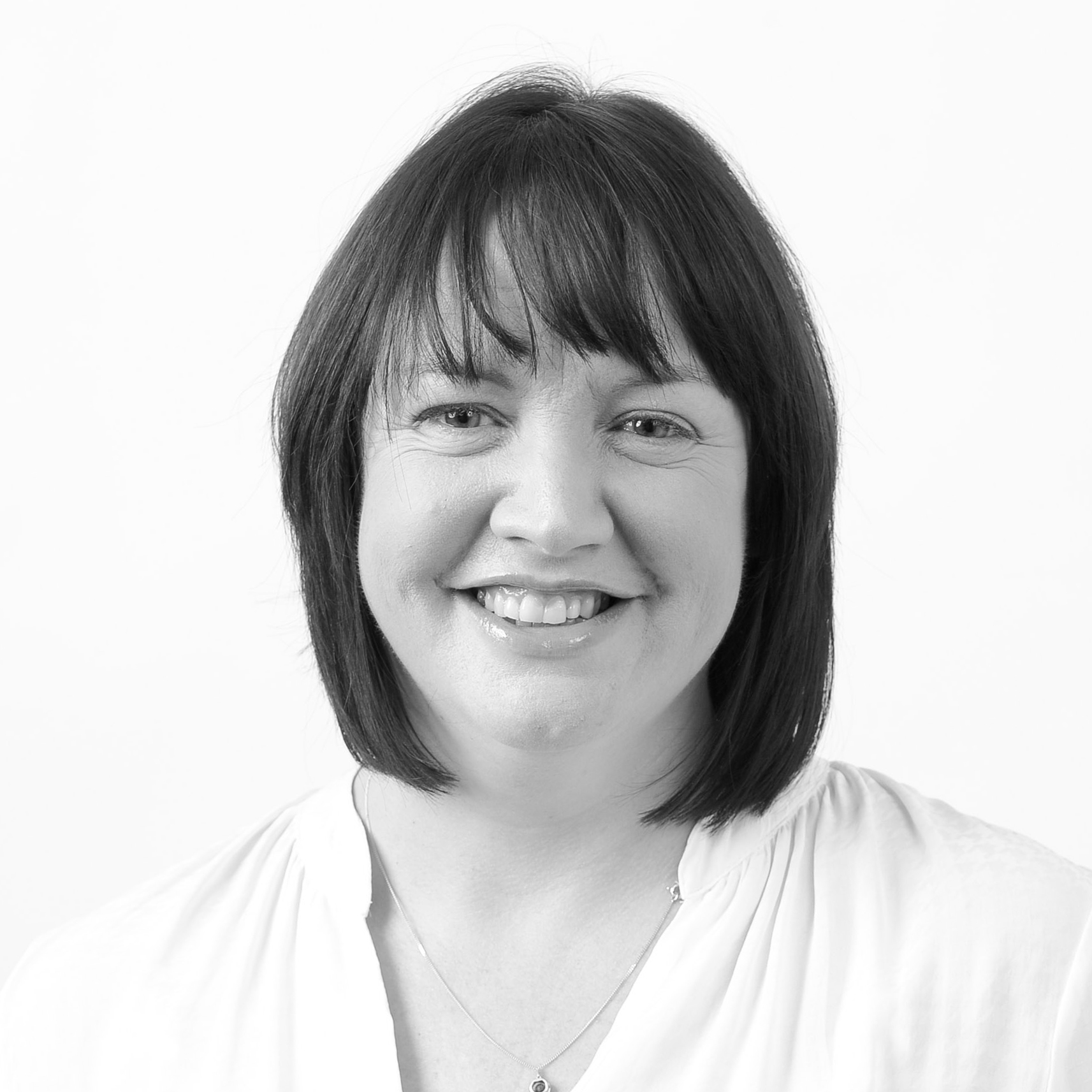 A black and white headshot image of a smiling woman against a white backdrop