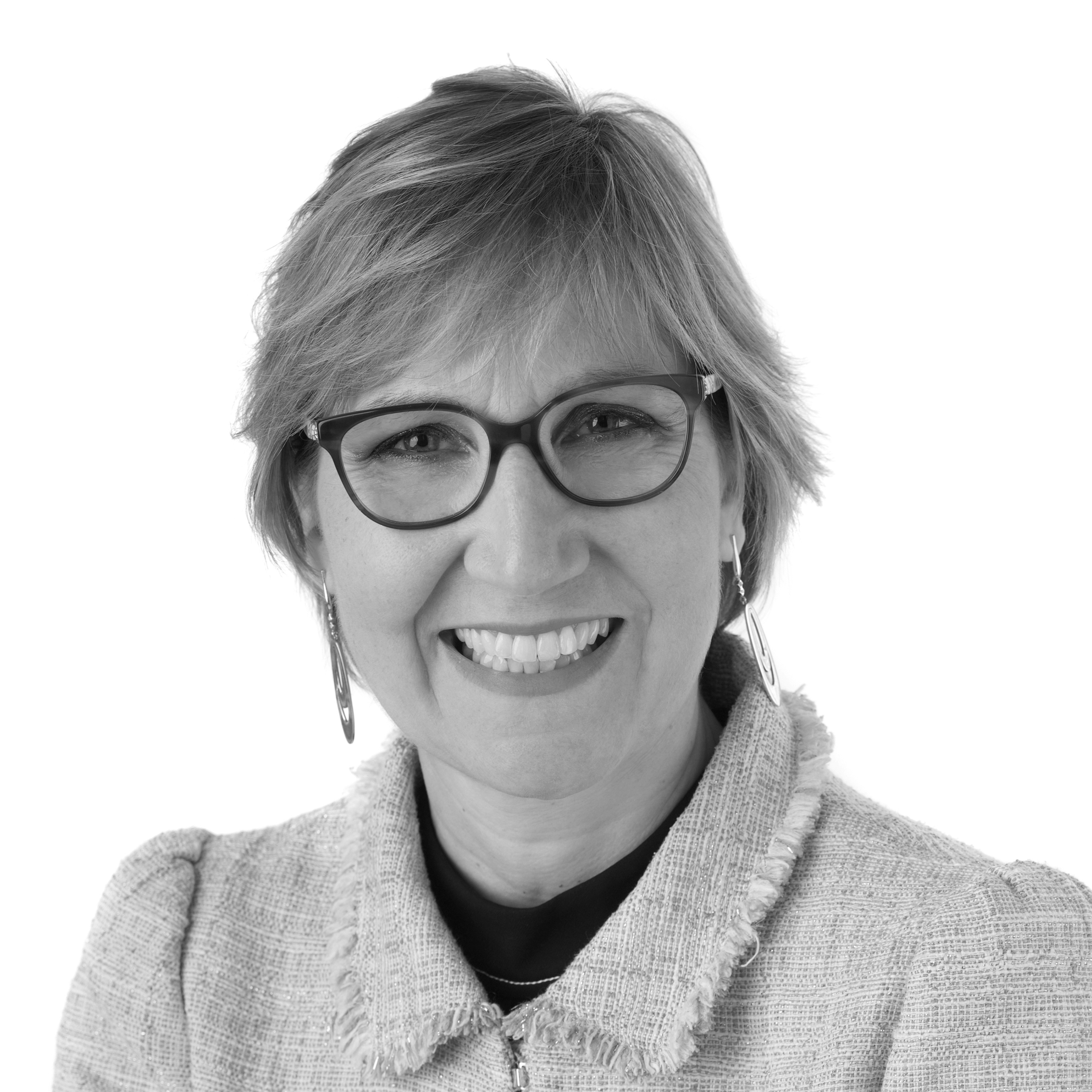 A black and white headshot image of a smiling woman with glasses against a white backdrop
