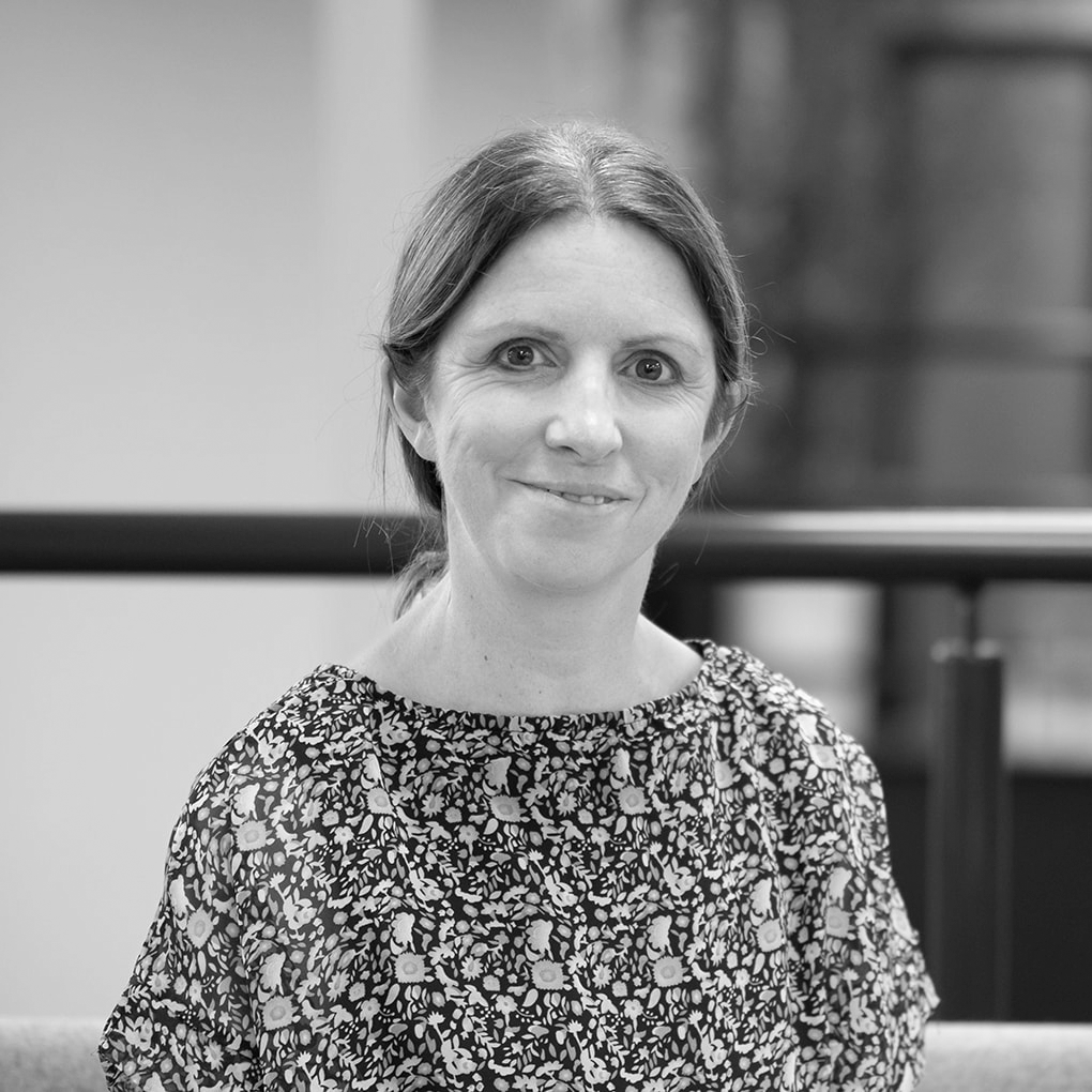 A black and white headshot image of a smiling woman against a white backdrop