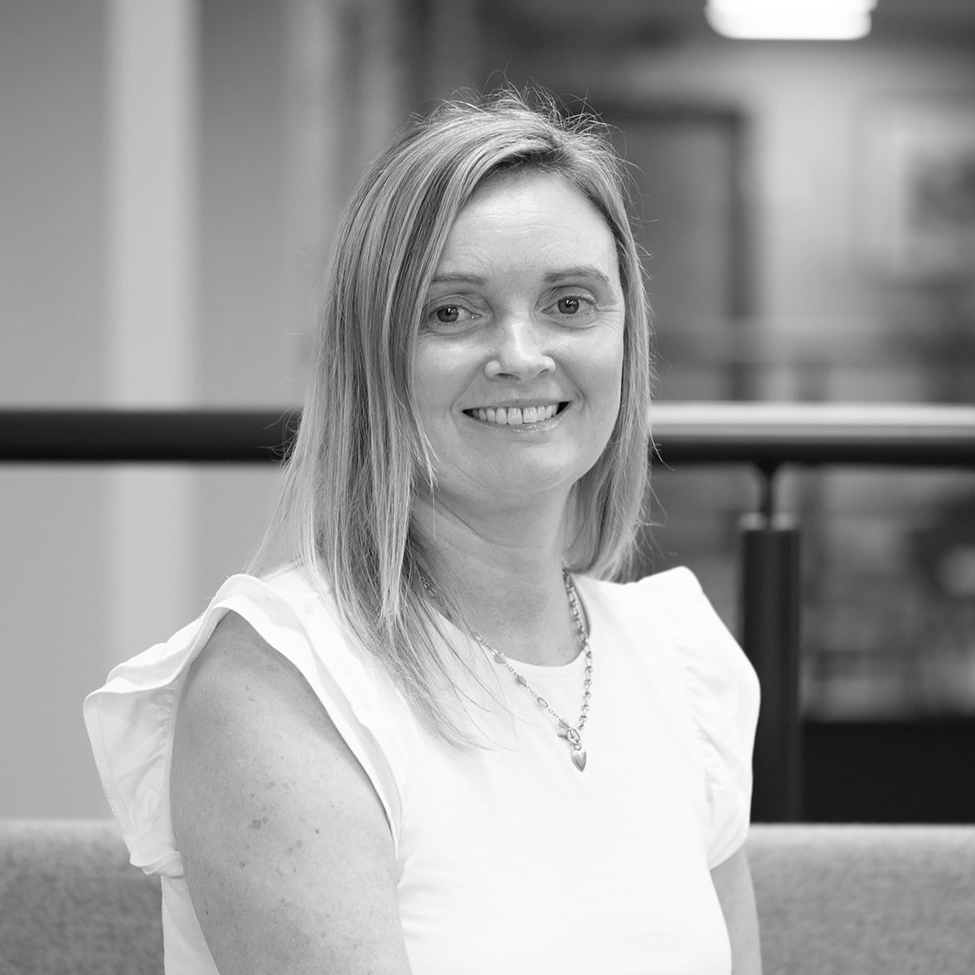 A black and white headshot image of a smiling woman against a white backdrop