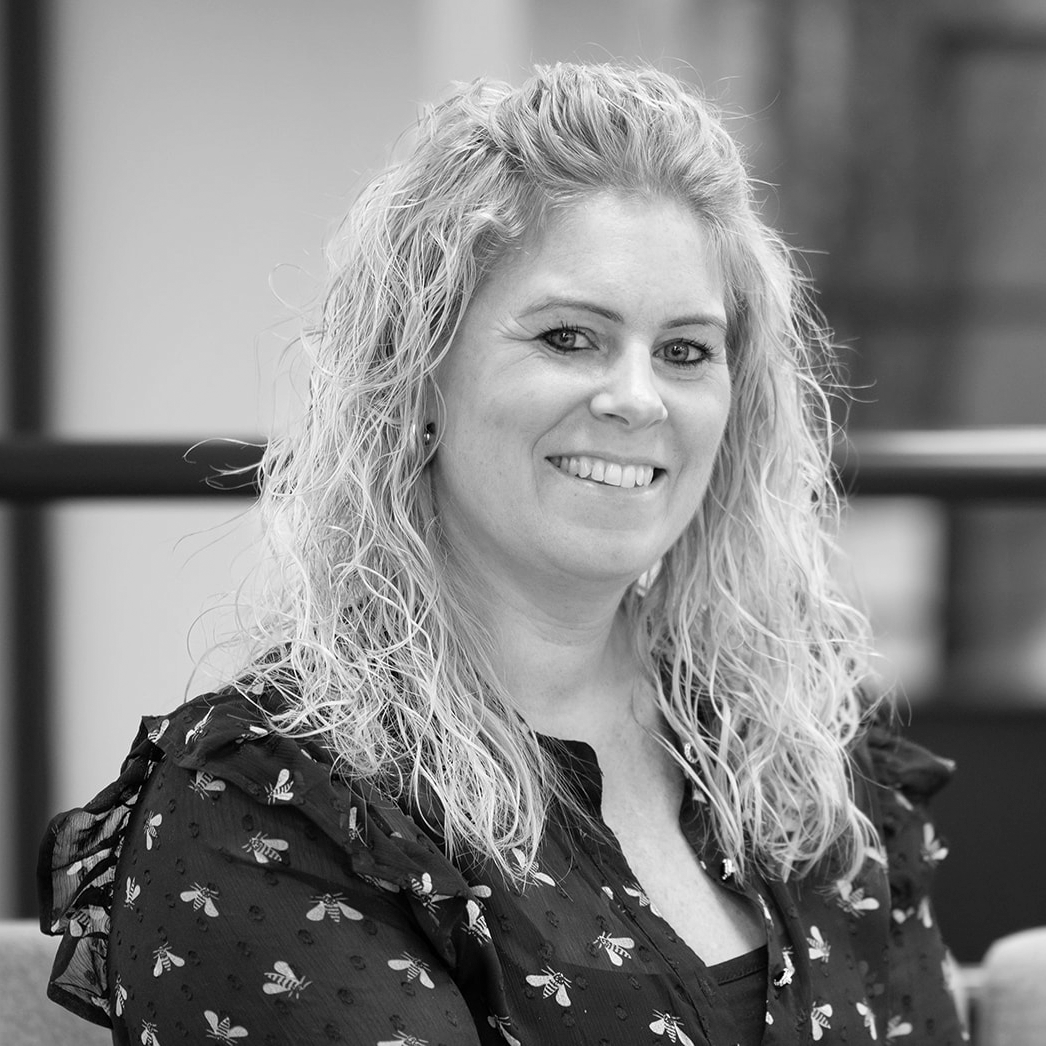 A black and white headshot image of a smiling woman against a white backdrop