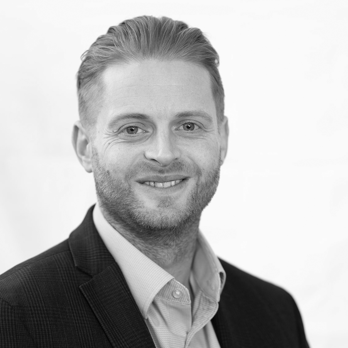 A black and white headshot image of a smiling man against a white backdrop