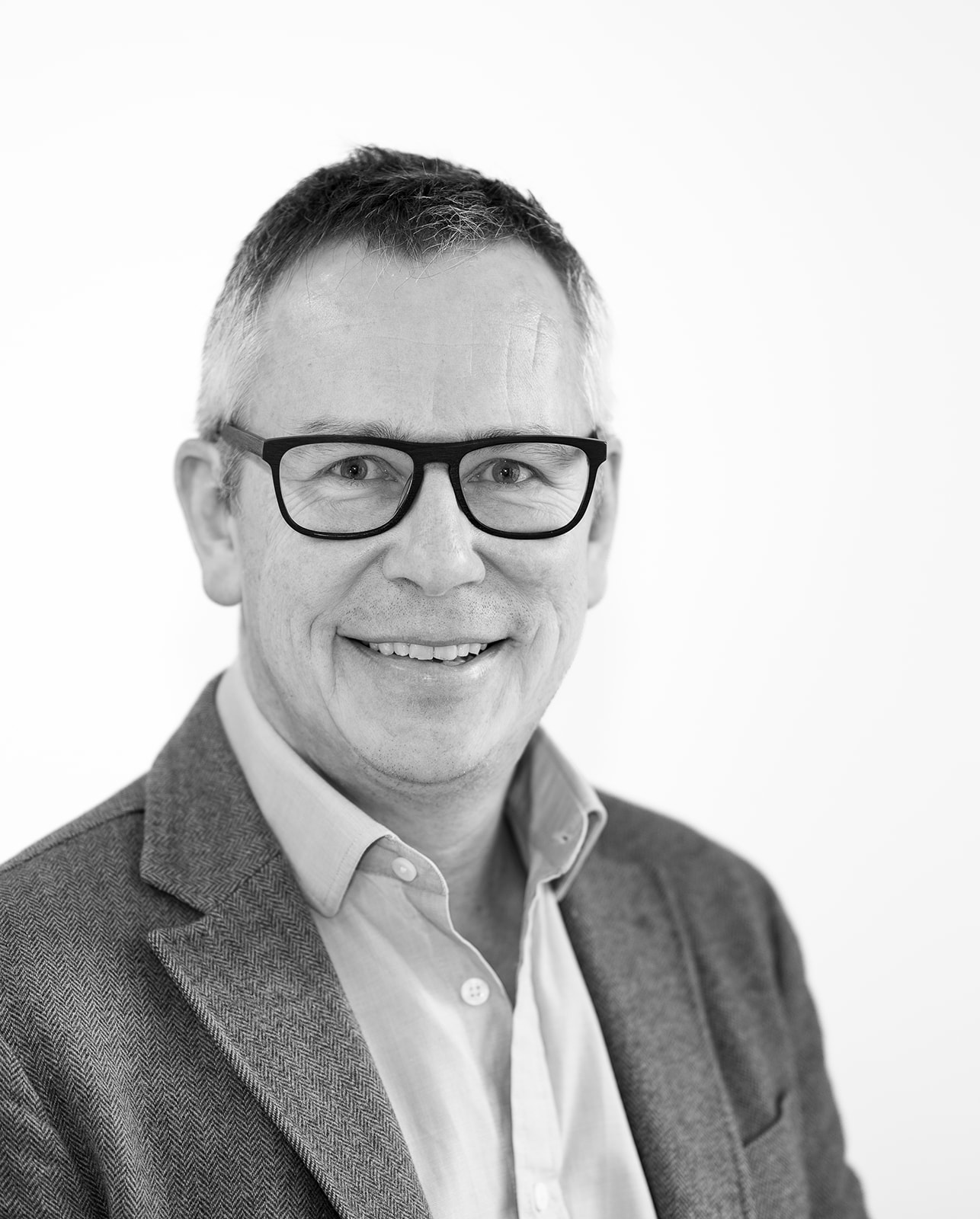 A black and white headshot image of a smiling man against a white backdrop