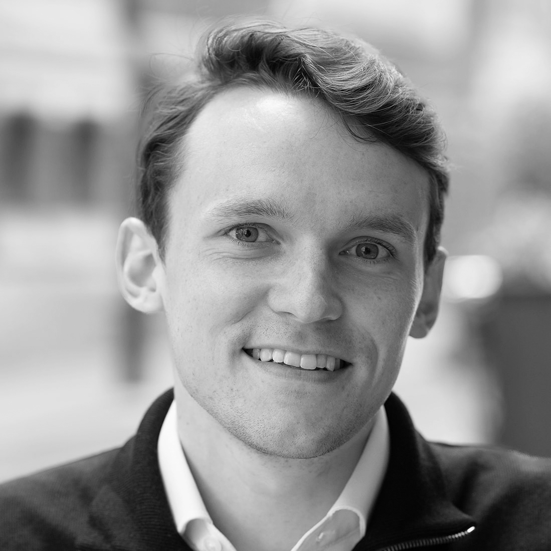 A black and white headshot image of a smiling man against a white backdrop