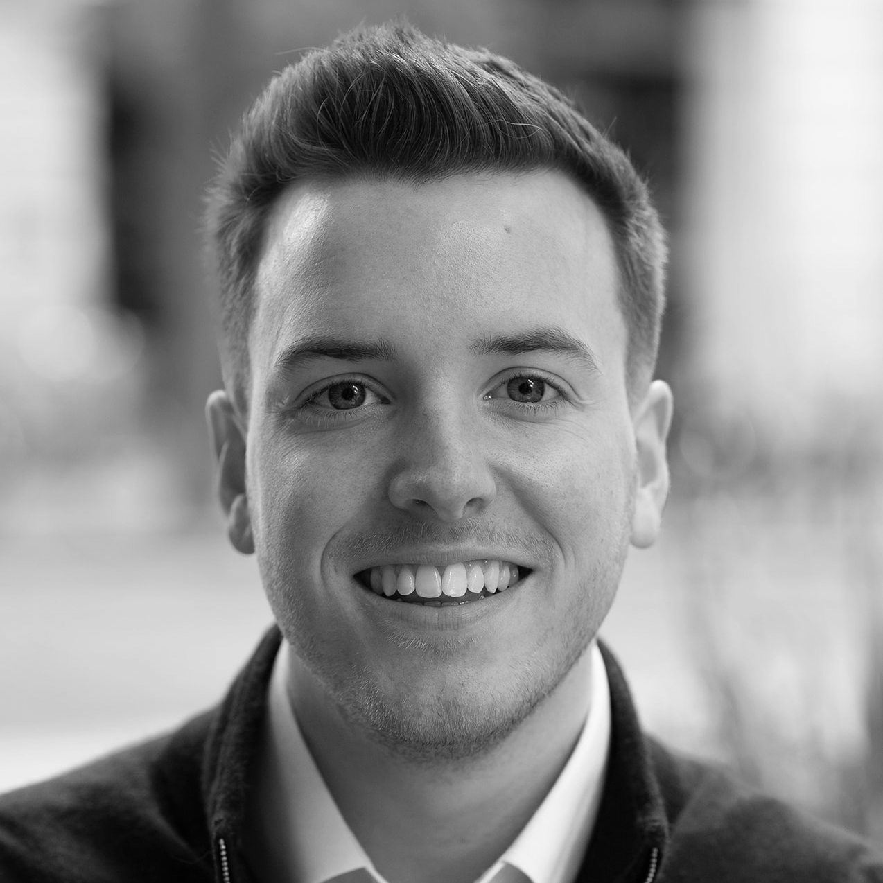 A black and white headshot image of a smiling man against a garden backdrop