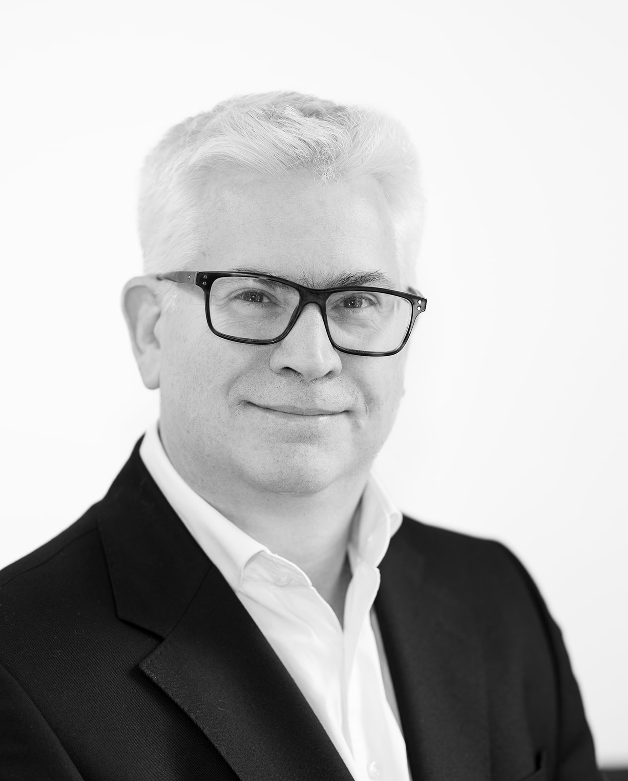 A black and white headshot image of a smiling man against a white backdrop