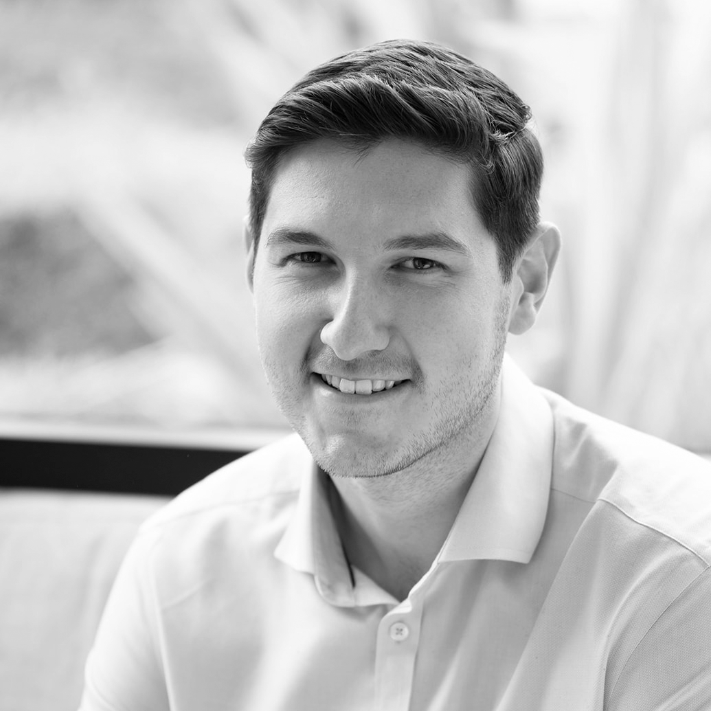 A black and white headshot image of a smiling man against a backdrop with a window.