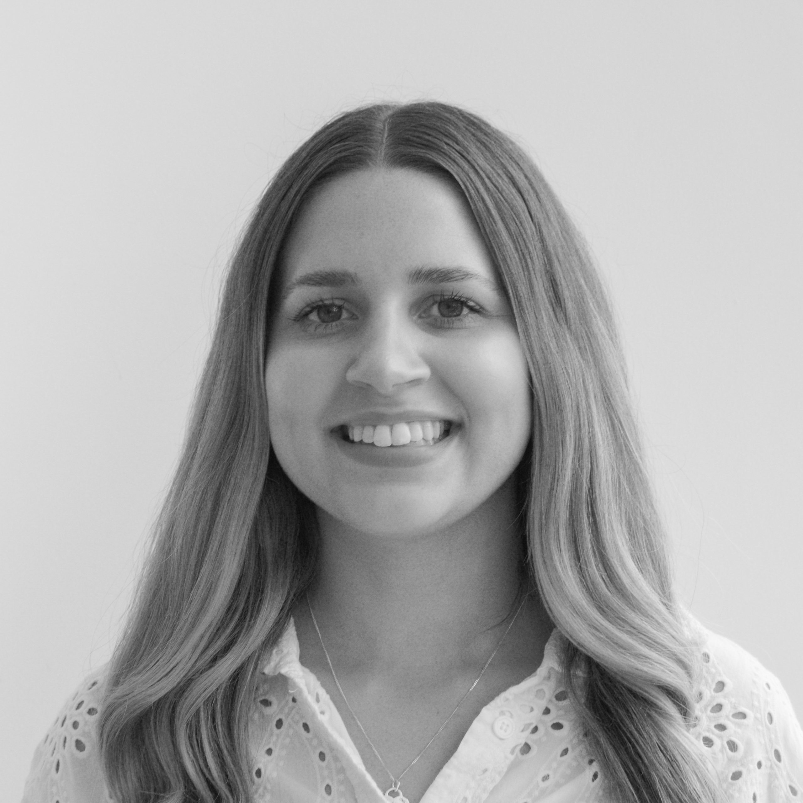 A black and white headshot image of a smiling woman against a white backdrop