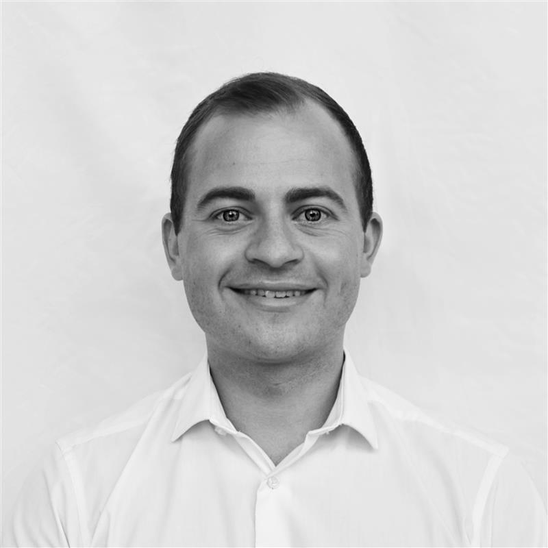 A black and white headshot image of a smiling man against a white backdrop