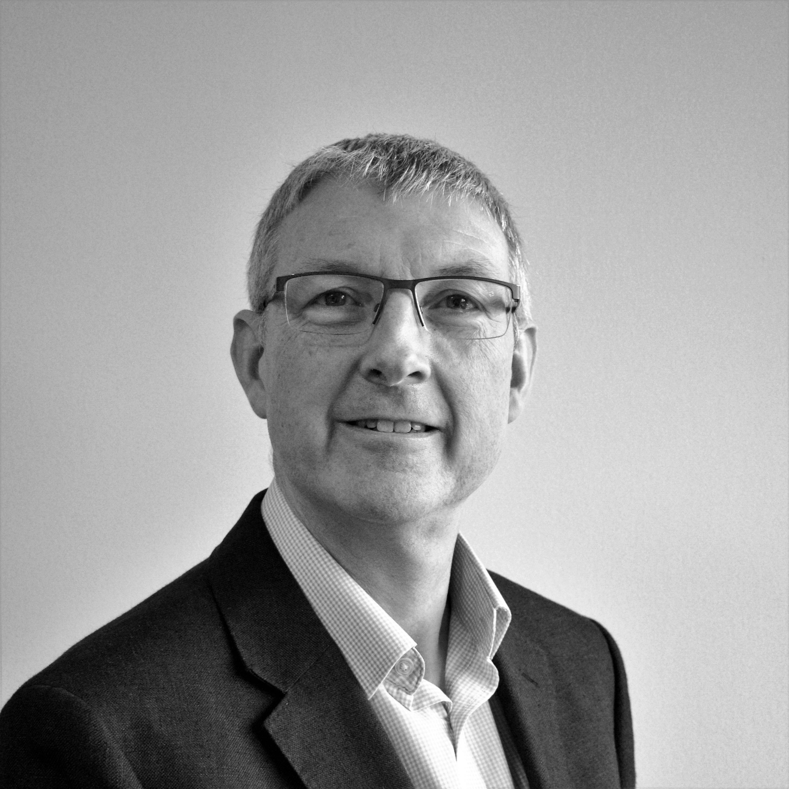 A black and white headshot image of a smiling man against a white backdrop