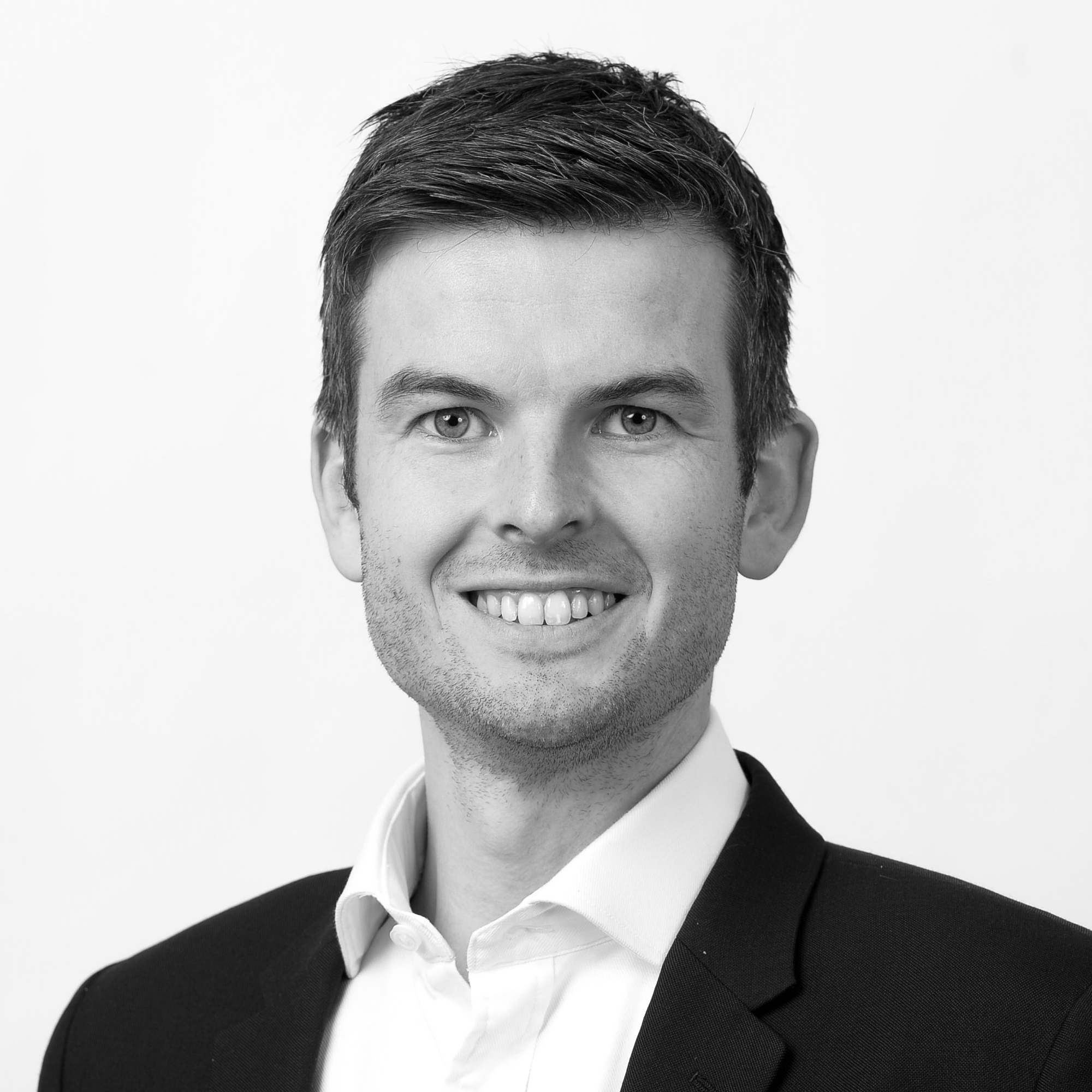 A black and white headshot image of a smiling man against a white backdrop
