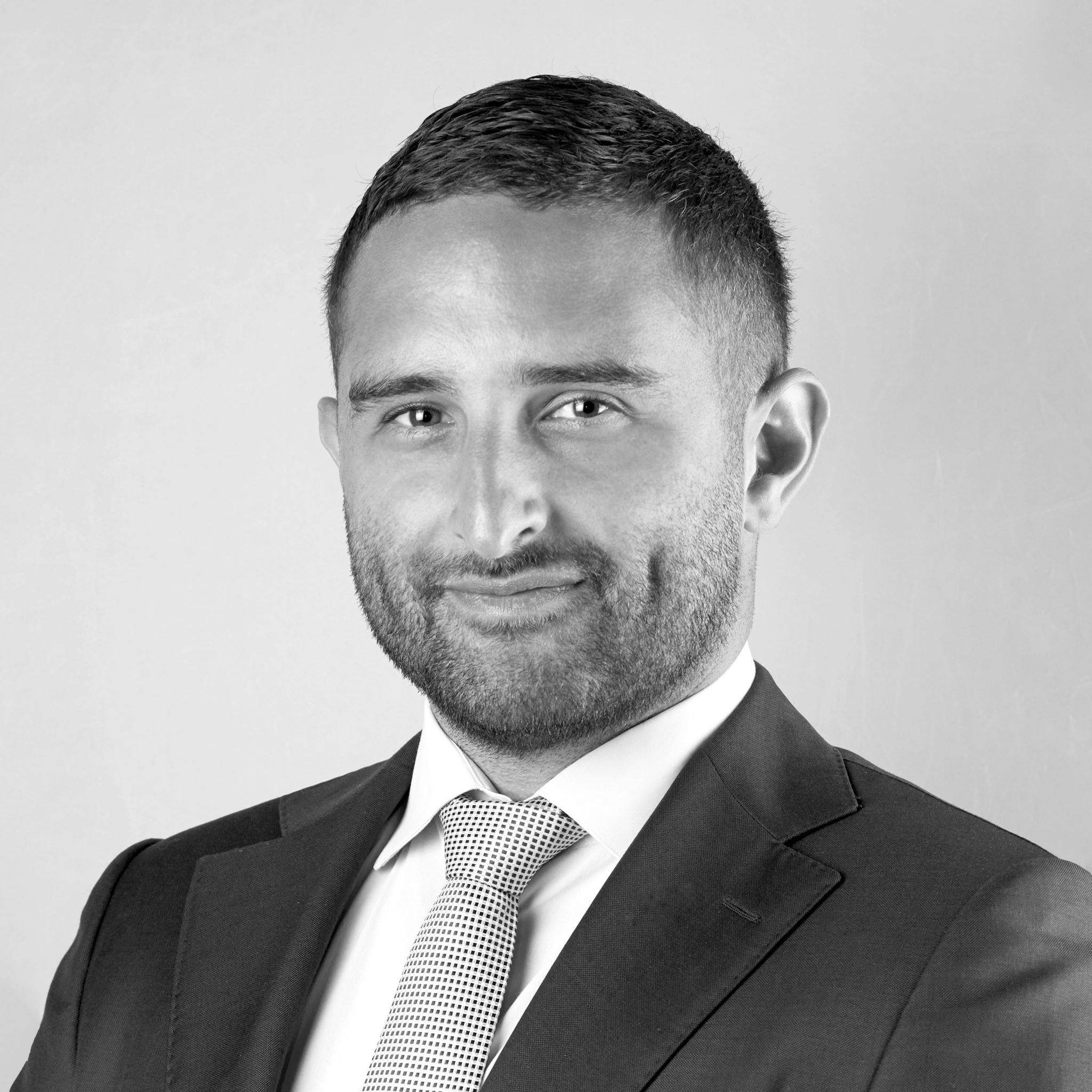 A black and white headshot image of a smiling man against a white backdrop