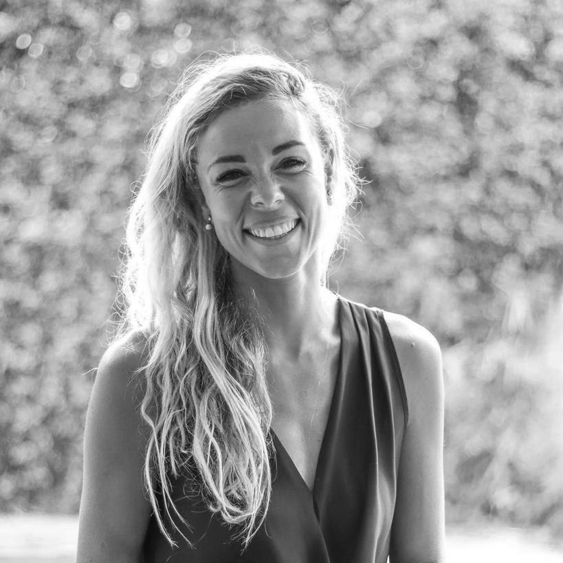 A black and white headshot image of a smiling woman against a blurred garden backdrop