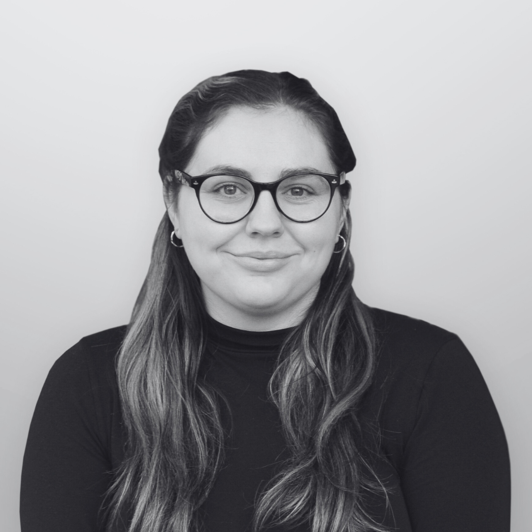 A black and white headshot image of a smiling woman with glasses against a white backdrop