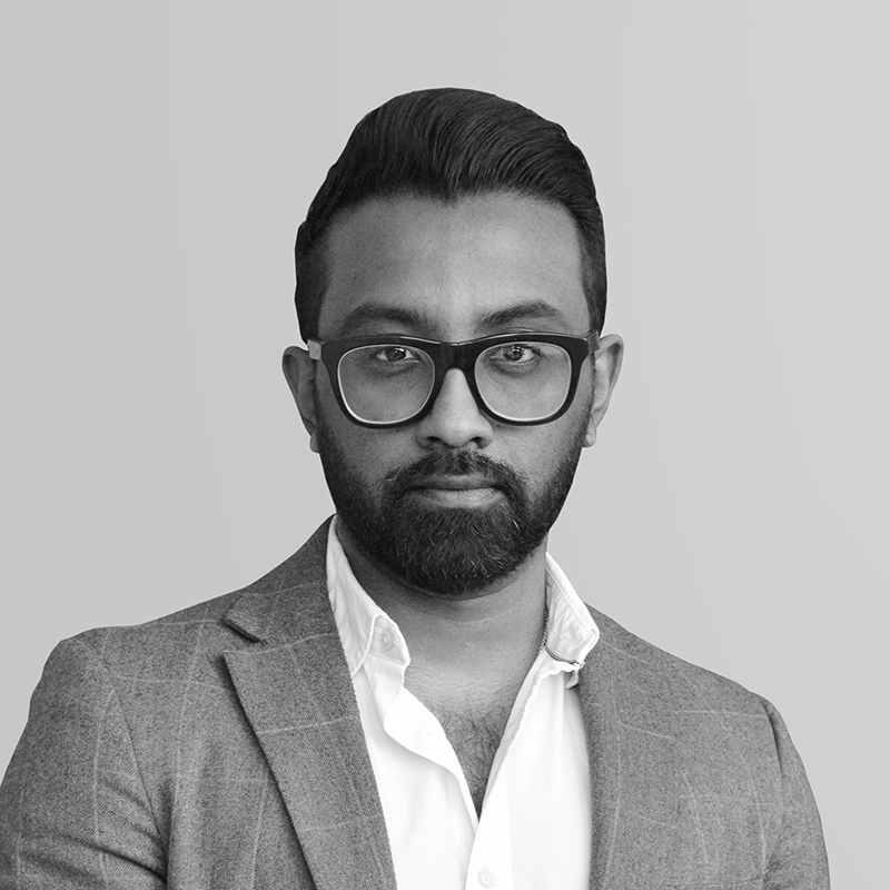 A black and white headshot image of a smiling man with glasses against a white backdrop
