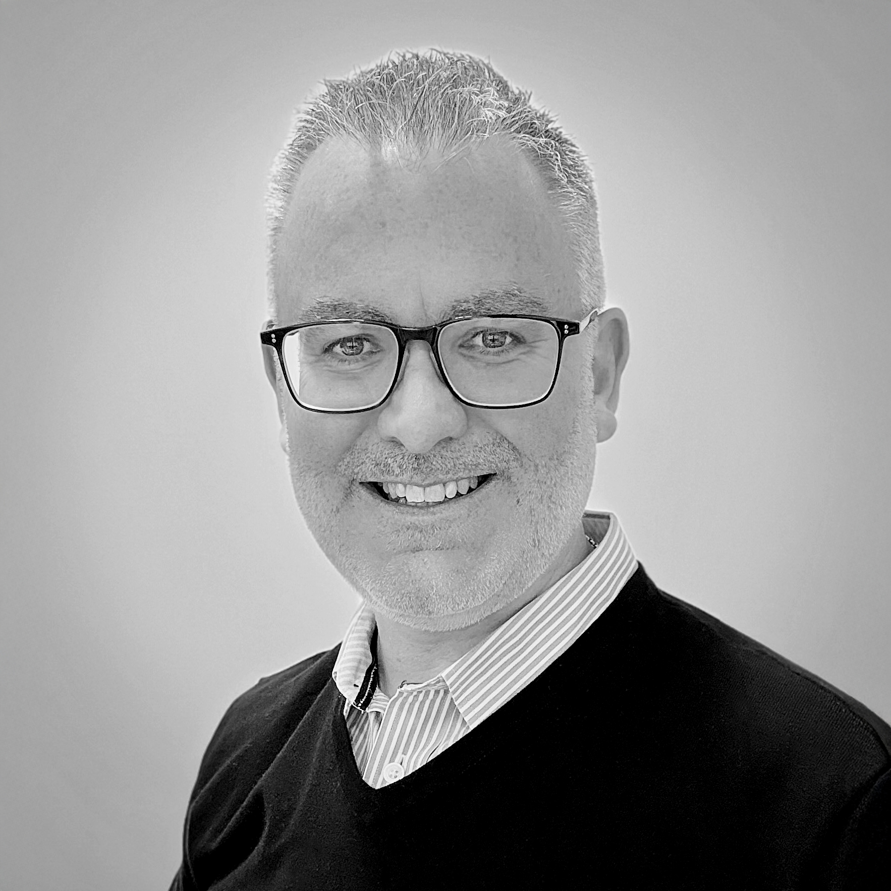A black and white headshot image of a smiling man against a white backdrop