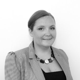 A black and white headshot image of a smiling woman against a white backdrop