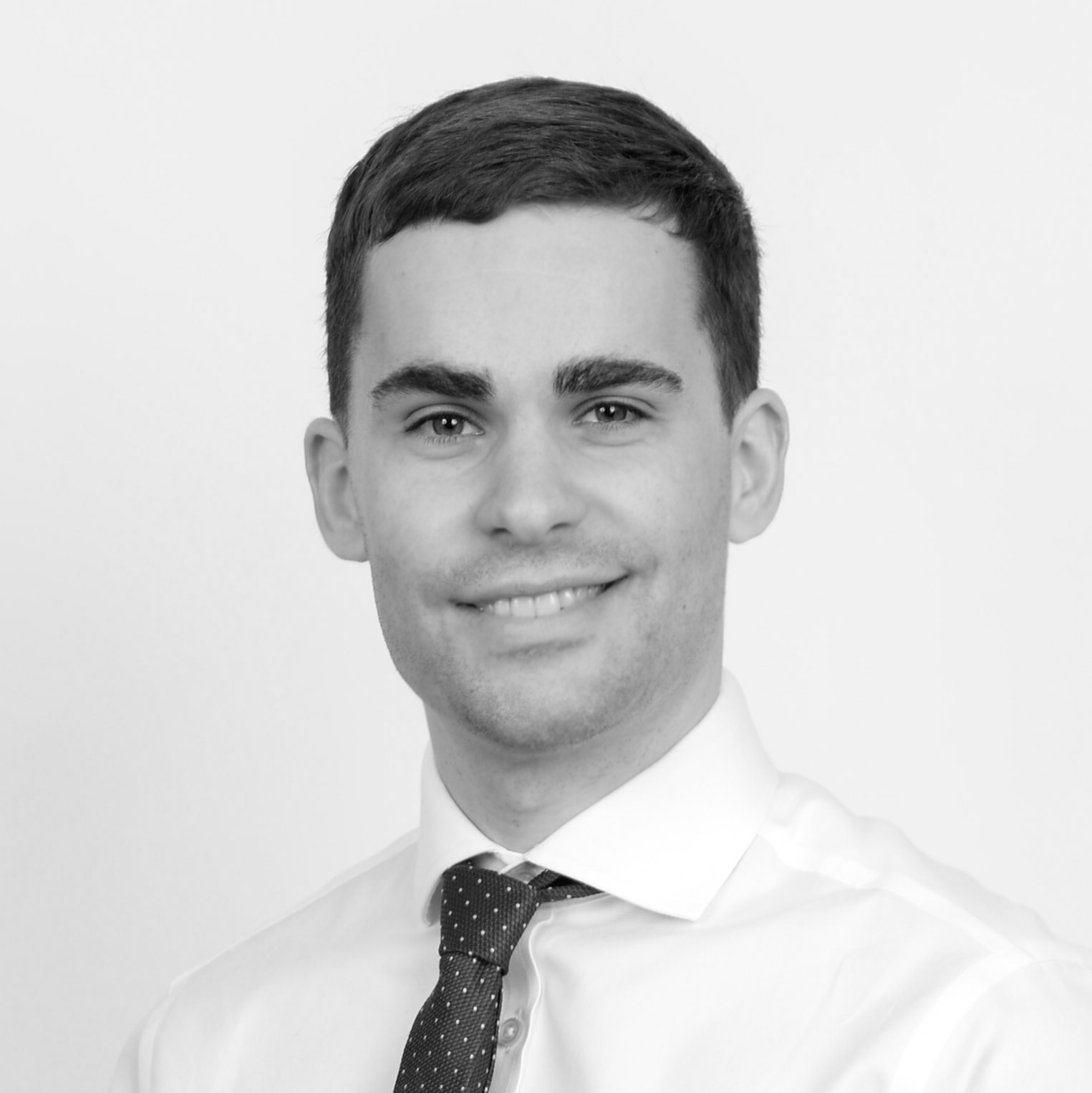 A black and white headshot image of a smiling man against a white backdrop