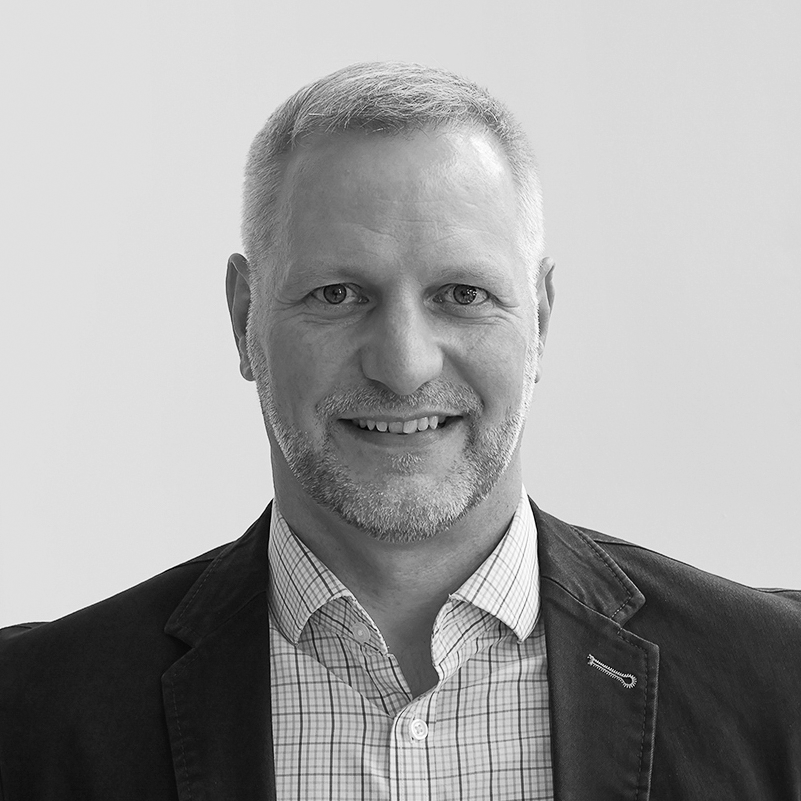 A black and white headshot image of a smiling man against a white backdrop