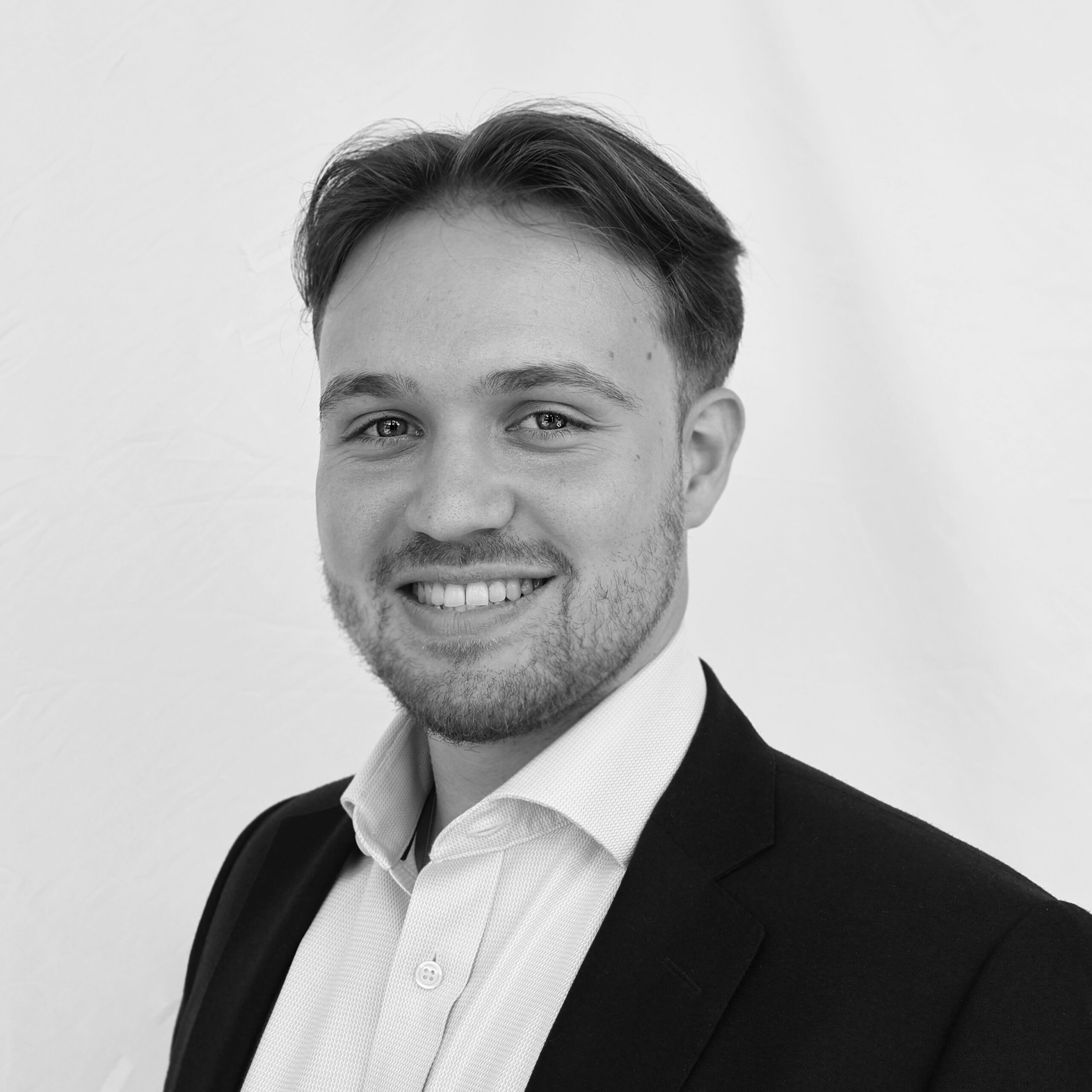 A black and white headshot image of a smiling man against a white backdrop