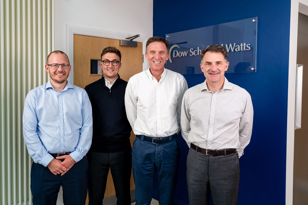 Three Bridgewood founders and James Dow, CEO of Dow Schofield Watts, smiling and posing for a photo in front of the company logo.