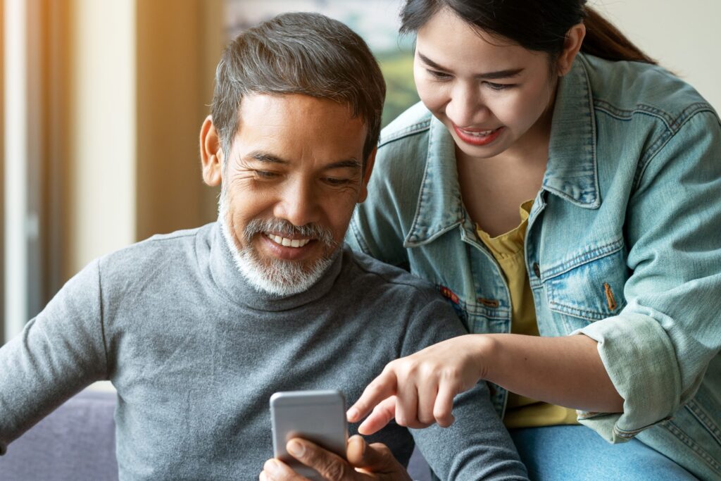 A smiling man with a grey beard and a woman looking at a smartphone together.