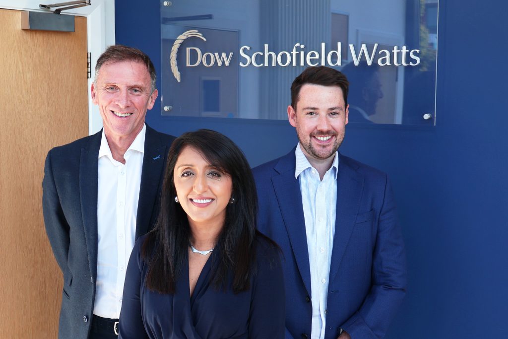 Co-founder, James Dow, CEO Shru Morris, and CFOO Pete Fendall standing together in front of the Dow Schofield Watts logo.