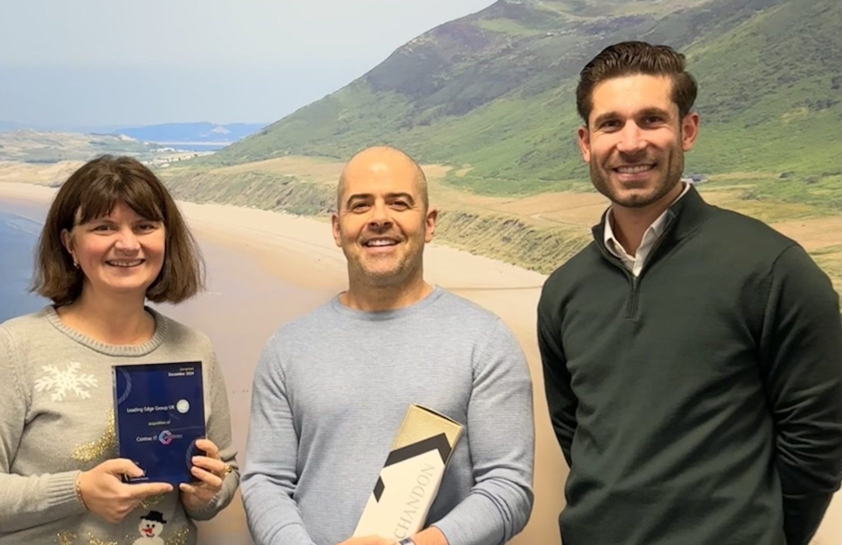 Koo Aseeley with Leading Edge smiling in front of a wall mural of a beach and grassy hills.