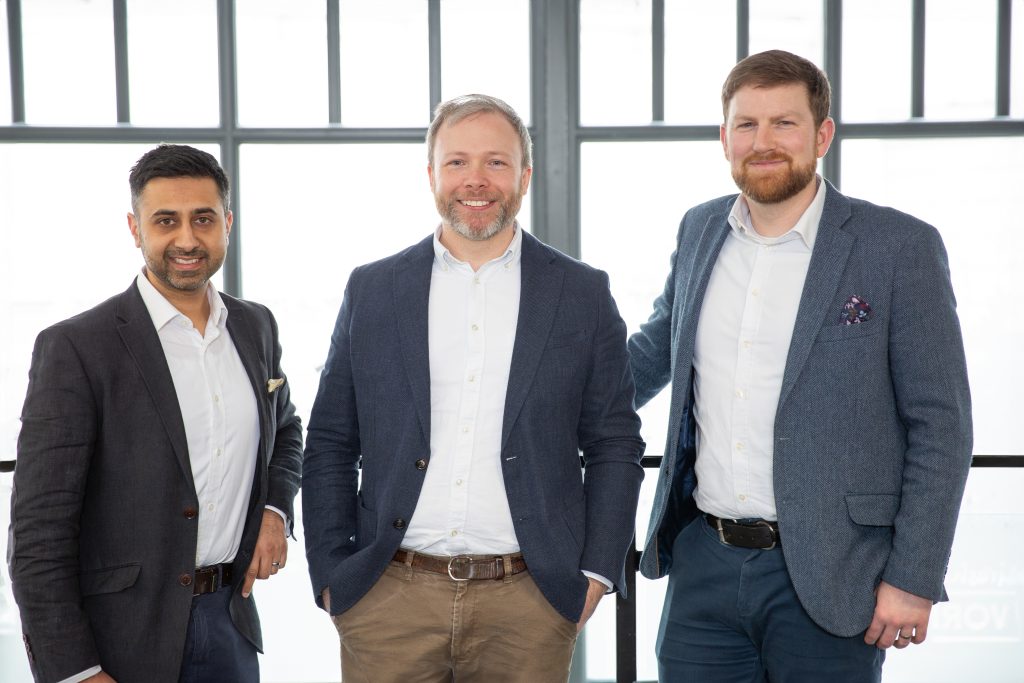 Three smiling male workers in an office building.