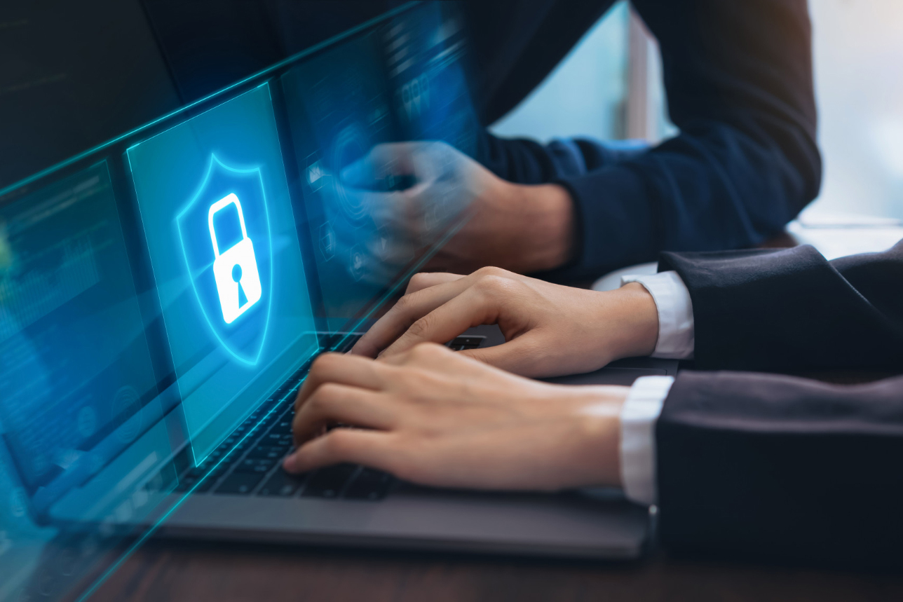 A person types on a laptop keyboard, with a glowing shield and lock icon on the screen. The icon symbolises data security or cybersecurity.