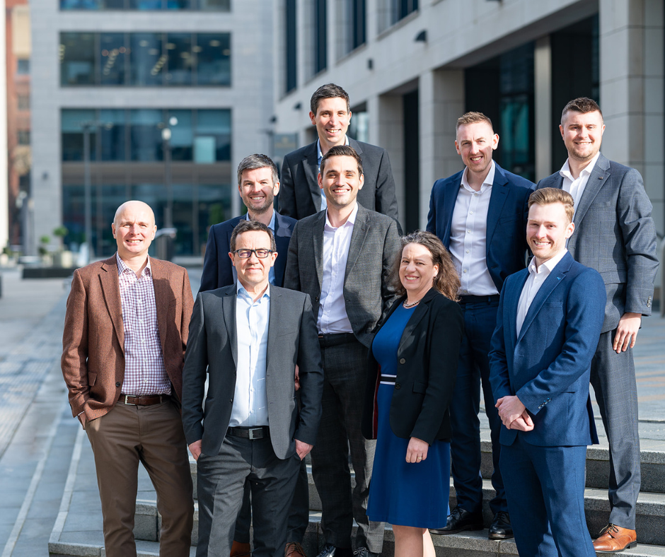 A professional photo of nine colleagues happy and confident standing outside in front of an office park.