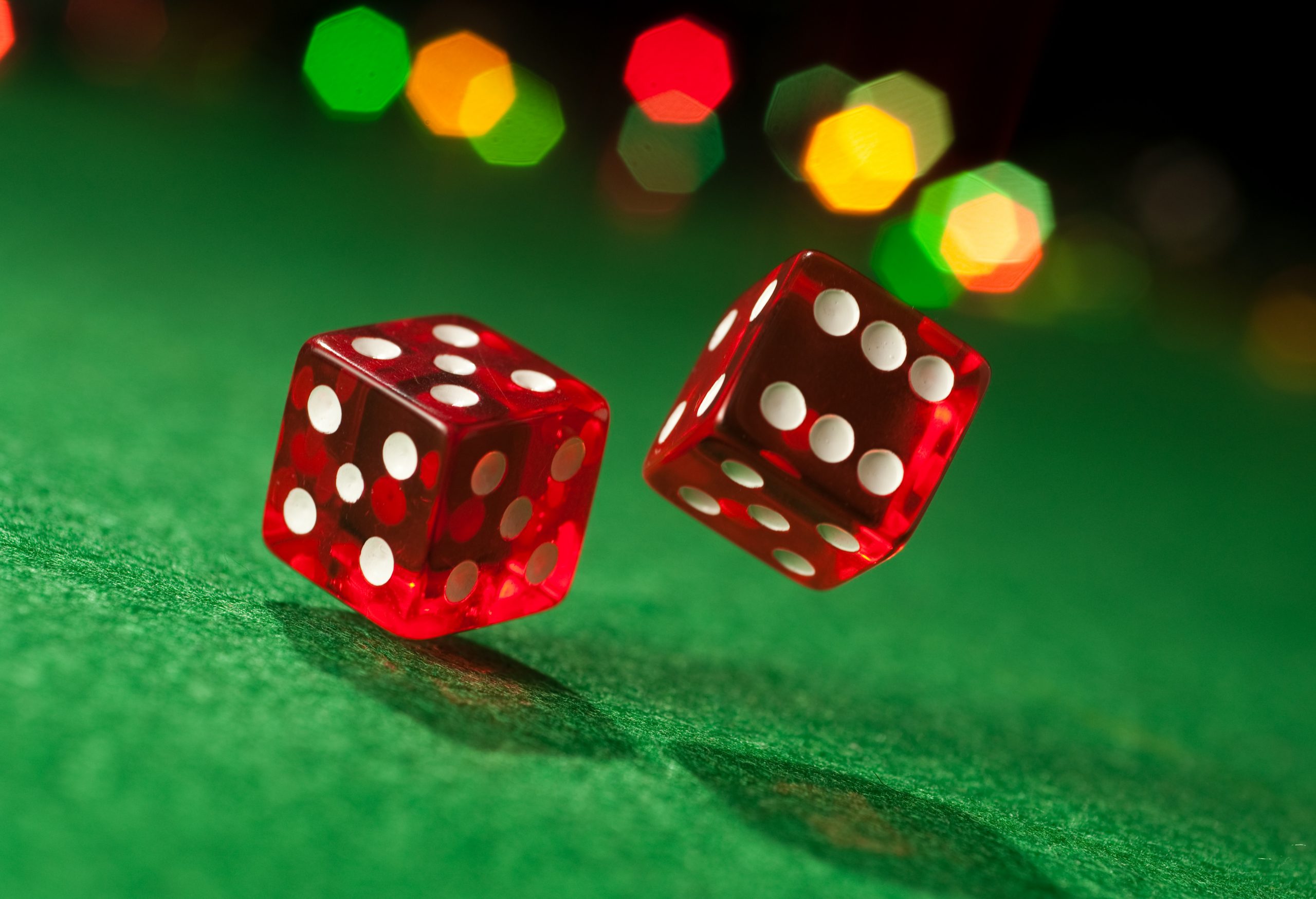 Two red dice with white spots are rolling on a green surface.
