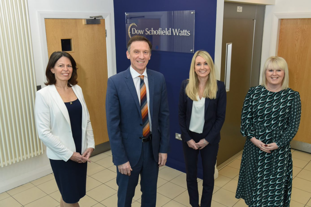 Three female and one male colleague stood smiling professionally in front of the Dow Schofield Watts logo