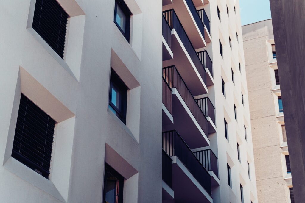 A modern apartment building with white facades, small balconies, and window blinds.