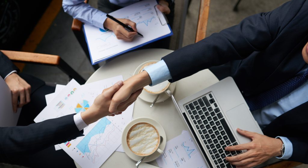 Two business partners shaking hands after closing a deal over coffee.